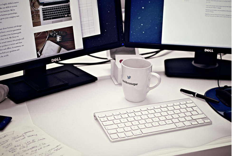 a coffee mug, a keyboard, a monitor on an office desk